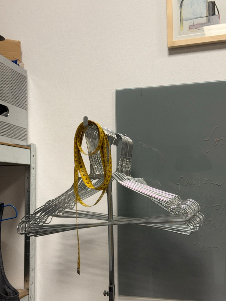Clear plastic hangers stacked on a metal rod with a measuring tape draped over them, against a white wall.