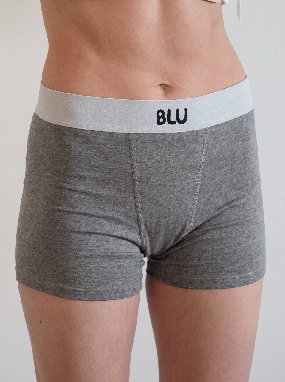 A close-up of a person wearing heather gray boxer briefs with a white waistband featuring the black text 'BLU'.