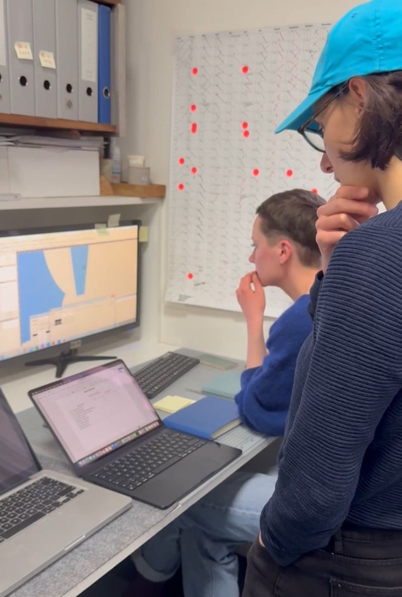 Two people working on laptops in a lab setting with a monitor displaying a map.